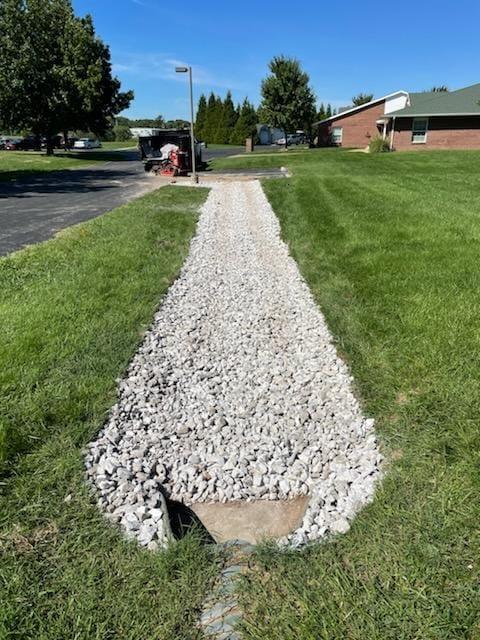 Original photograph: a completed surface French drain in a residential yard, with white gravel running from the home’s downspout area out across the lawn to redirect rainwater away from the foundation